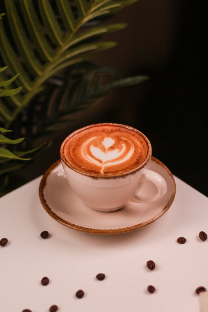 Elegant cappuccino with latte art surrounded by coffee beans on a white surface.