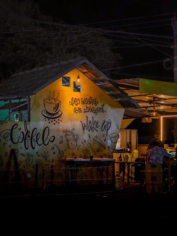 Warm and inviting coffee shop exterior with artistic wall mural at night.
