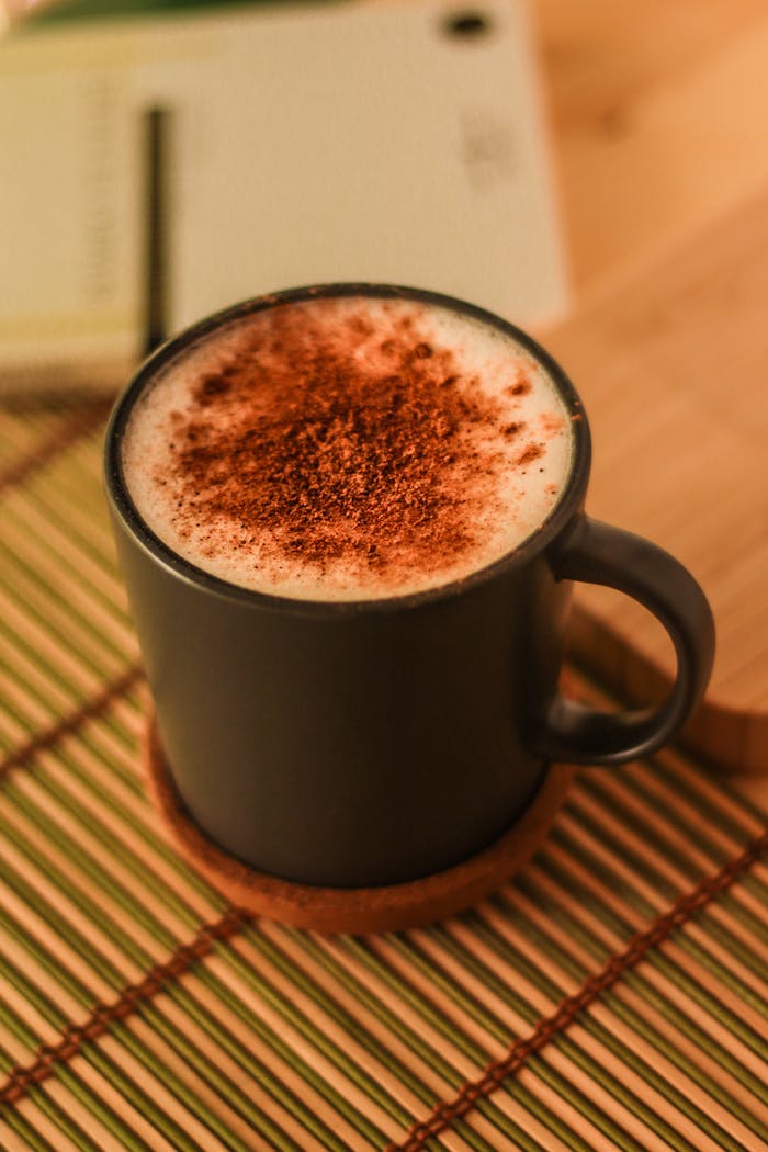 Warm cappuccino with cocoa powder in a black mug on a bamboo mat. Perfect for cozy mornings.